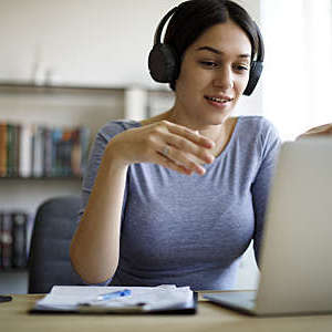 Close-up of young woman with headphones engaged in a video conference from home.