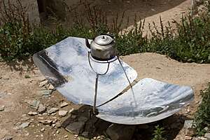 Close view of kettle heating on a solar stove set up on dusty, stony ground. (Ganden Monastery, Tibet)